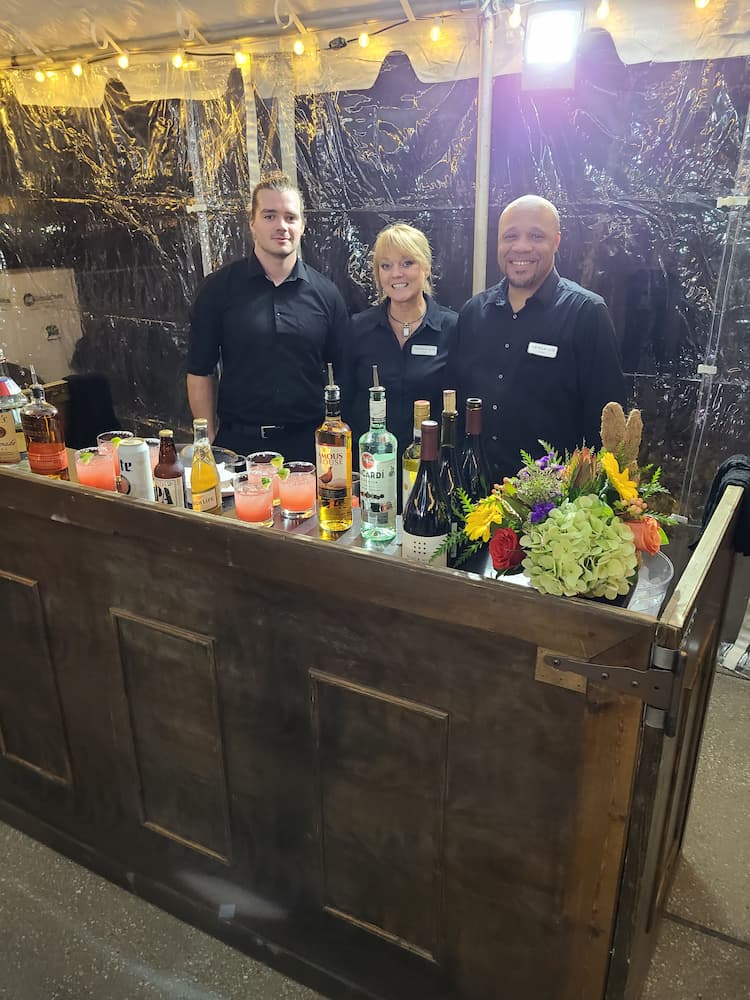 Three bartenders at an event with bottles of alcohol